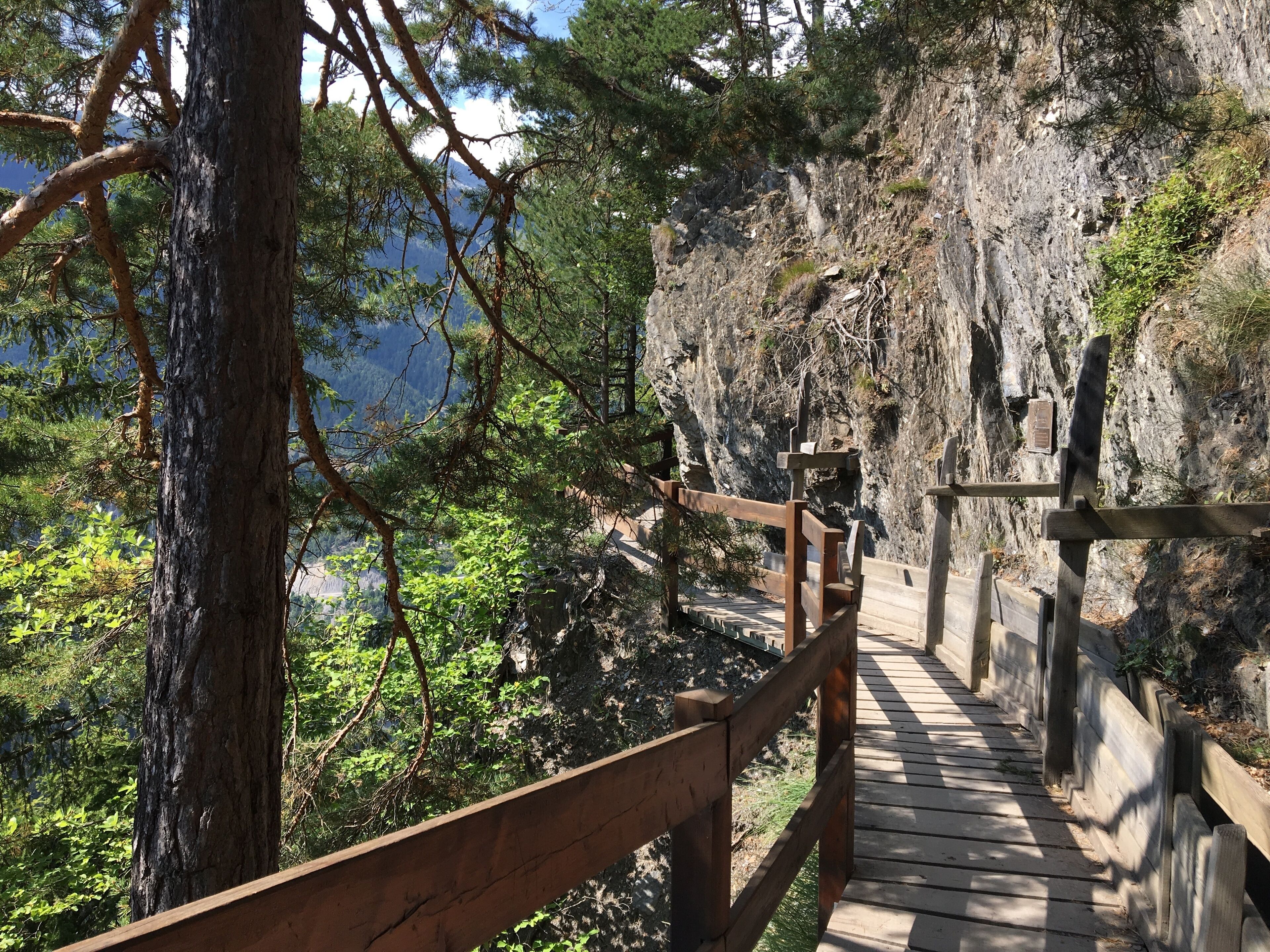 Un sentier en bois qui monte le long d’une falaise rocheuse, entouré d’arbres et de verdure.