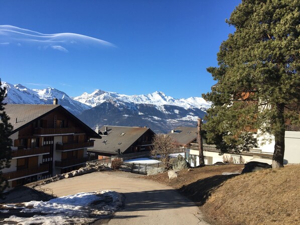 A mountain lodge with a view of snow-capped peaks, a paved driveway, and a wooden building with a balcony. - IRIS Apartment "Vacation Rental in Veysonnaz, 4 Valleys" (Veysonnaz)