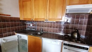 A compact kitchen with wooden cabinets, a built-in dishwasher, a sink, and a kettle. - IRIS Apartment "Vacation Rental in Veysonnaz, 4 Valleys" (Veysonnaz)