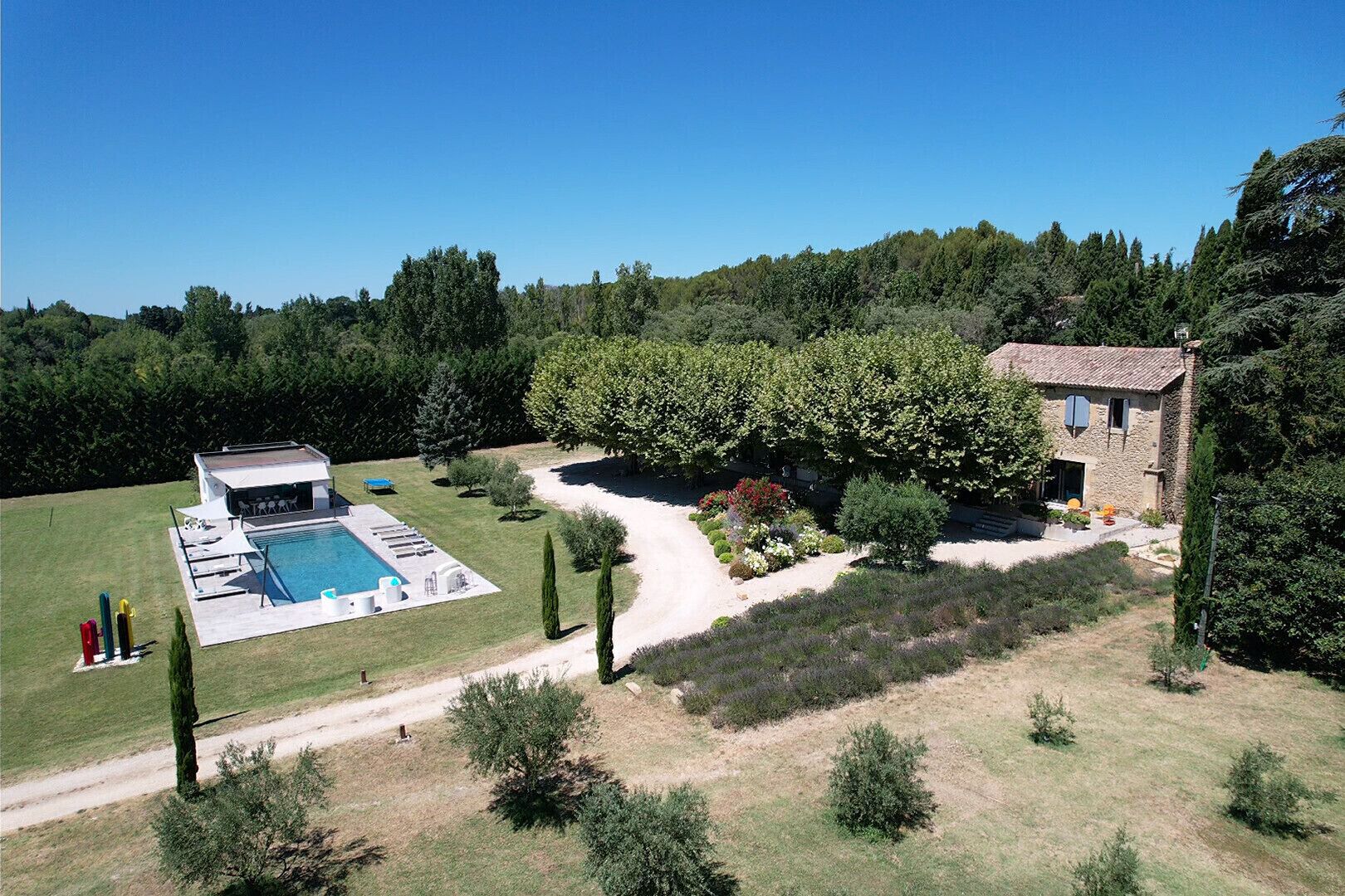 A large house with a swimming pool, a garden, and a forested area in the background.