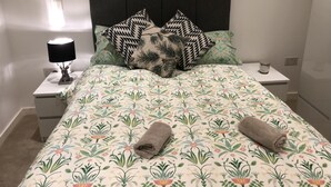 A neatly made bed with floral bedding, two pillows, and two rolled towels. - Luxury 2 Bed 2 Bath Apartments next to kings cross (London)