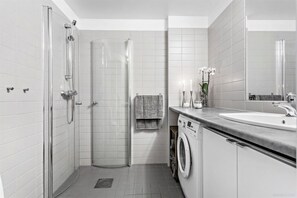 A modern bathroom with a glass shower enclosure, a built-in washing machine, and a large mirror.