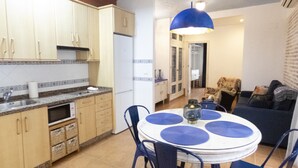 Cocina compacta con comedor, que incluye una mesa redonda con individuales azules, una lámpara colgante azul y un refrigerador.