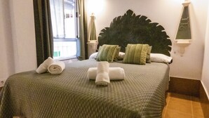 Una cama bien tendida con toallas enrolladas, un cabecero decorativo grande y vistas al exterior a través de una ventana.