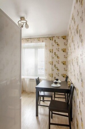 A compact dining area with a table and chairs, featuring a window with a white curtain and patterned wallpaper.