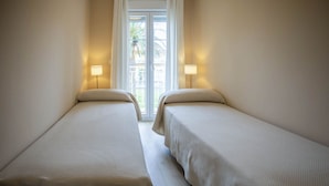 Habitación de hotel con dos camas individuales, una ventana con cortinas y dos lámparas de noche.