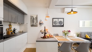 Cozinha moderna com armários brancos, uma ilha central e um espaço de refeições com um sofá e cadeiras cinzas.