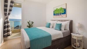 Quarto com cama, mesa de cabeceira, janela com cortinas, planta e um quadro na parede.