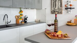 Uma cozinha moderna com bancada de mármore, uma garrafa de vinho, copos e uma tábua de madeira com comida e queijo.