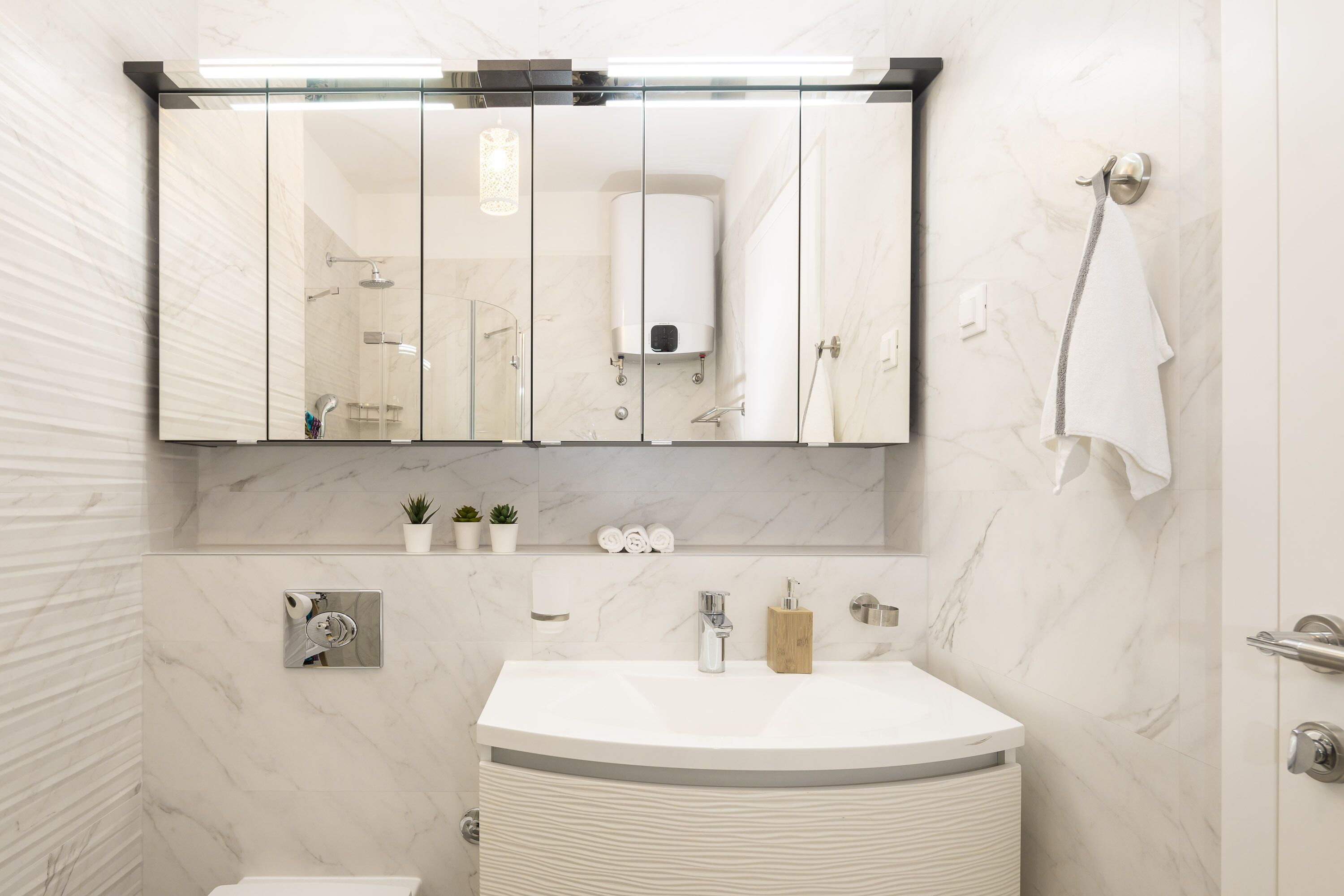 A modern bathroom with a large mirror, a white sink, and a towel hanging on the wall.