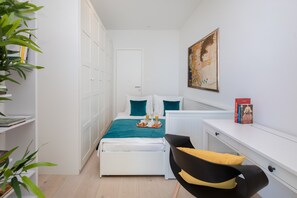 A modern hotel room with a bed, a desk, and a chair. There is a bookshelf with books and a plant. - Sun Spalato Sky (Split)