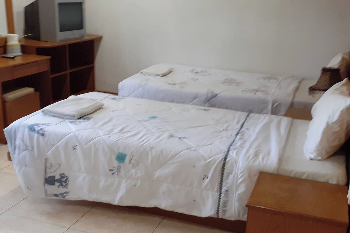 Una habitación con dos camas, un escritorio de madera con televisor y una mesita de noche de madera.