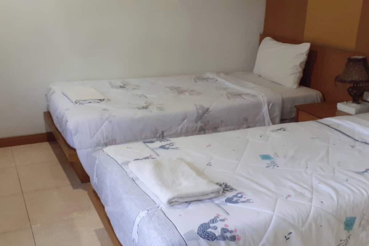 A hotel room with two single beds, each with a white bedspread and a folded white towel.