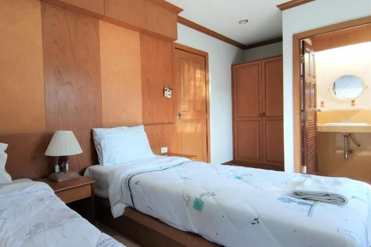 A hotel room with two beds, wooden paneling, a nightstand with a lamp, and a bathroom with a sink and mirror.