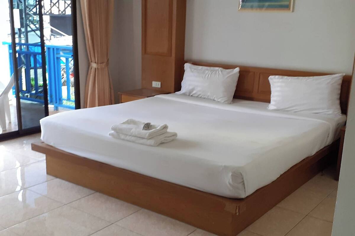 A hotel room with a large bed, a wooden headboard, and a view of a blue balcony.