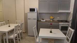 A compact kitchen with white cabinetry, a microwave, a refrigerator, a sink, and a stove. There are two white dining tables with chairs. - Mamamia City (Palermo)