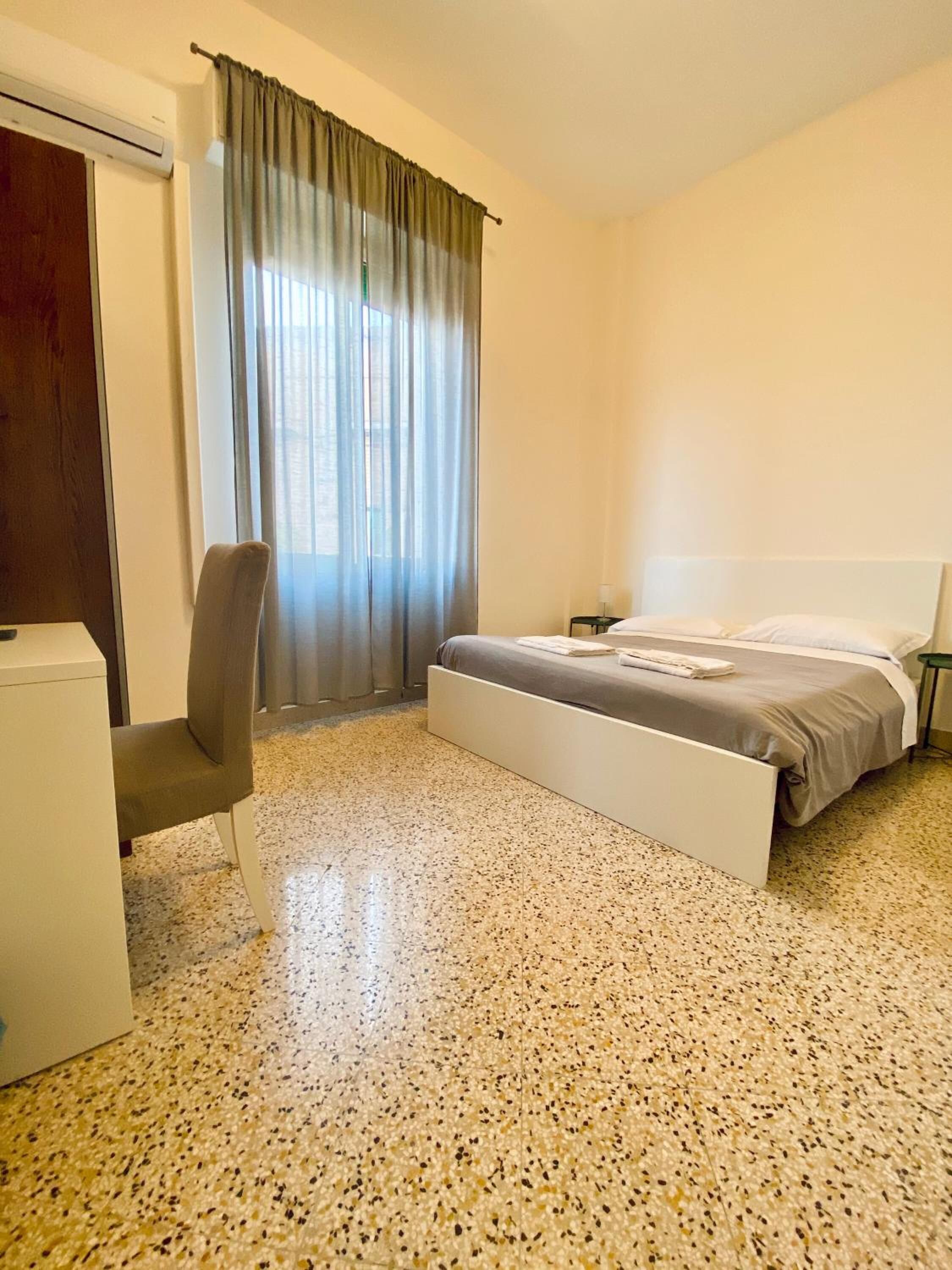 Une chambre à coucher avec un lit, une chaise, un bureau et une fenêtre avec des rideaux.