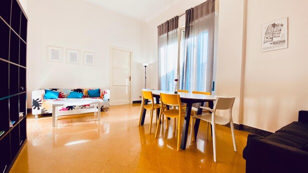 A modern living room with a sofa, dining table, and chairs. There is a door and a window with curtains. - Mamamia City (Palermo)