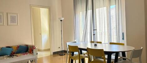 A room with a dining table, chairs, a sofa, and a floor lamp.