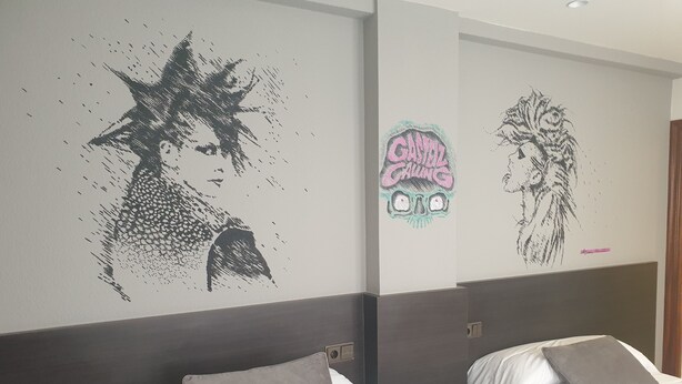 A hotel room with two beds, each with a grey pillow and a remote control on the nightstand. - Hotel Arts-Gasteiz (Vitoria-Gasteiz)