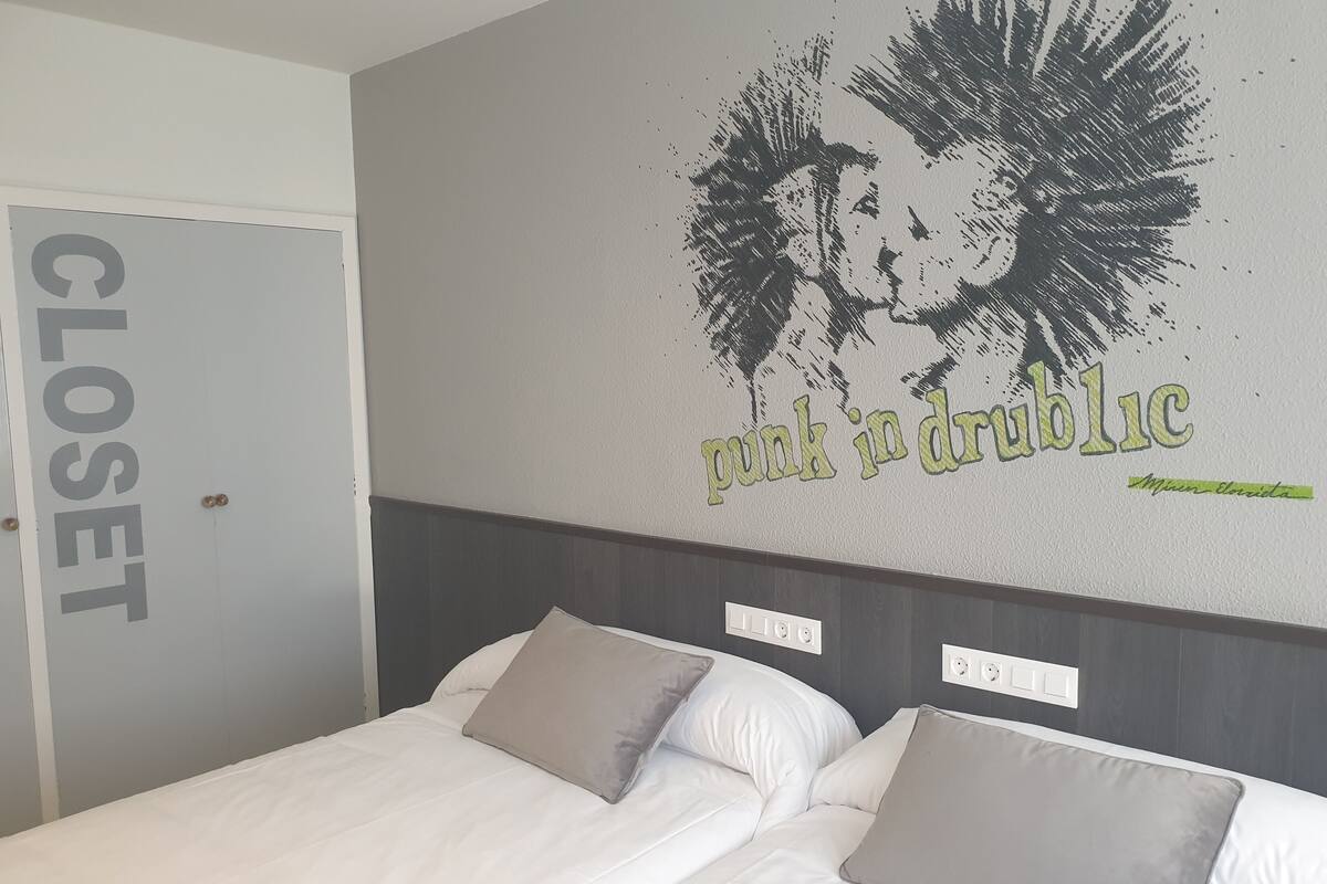 Habitació d'hotel amb un llit, dos coixins, una paret amb una imatge i text, i una porta d'armari.