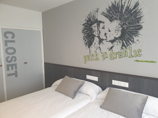 Une chambre d’hôtel avec un lit, deux oreillers, un mur orné d’un motif graphique et d’un texte, et une porte de placard.