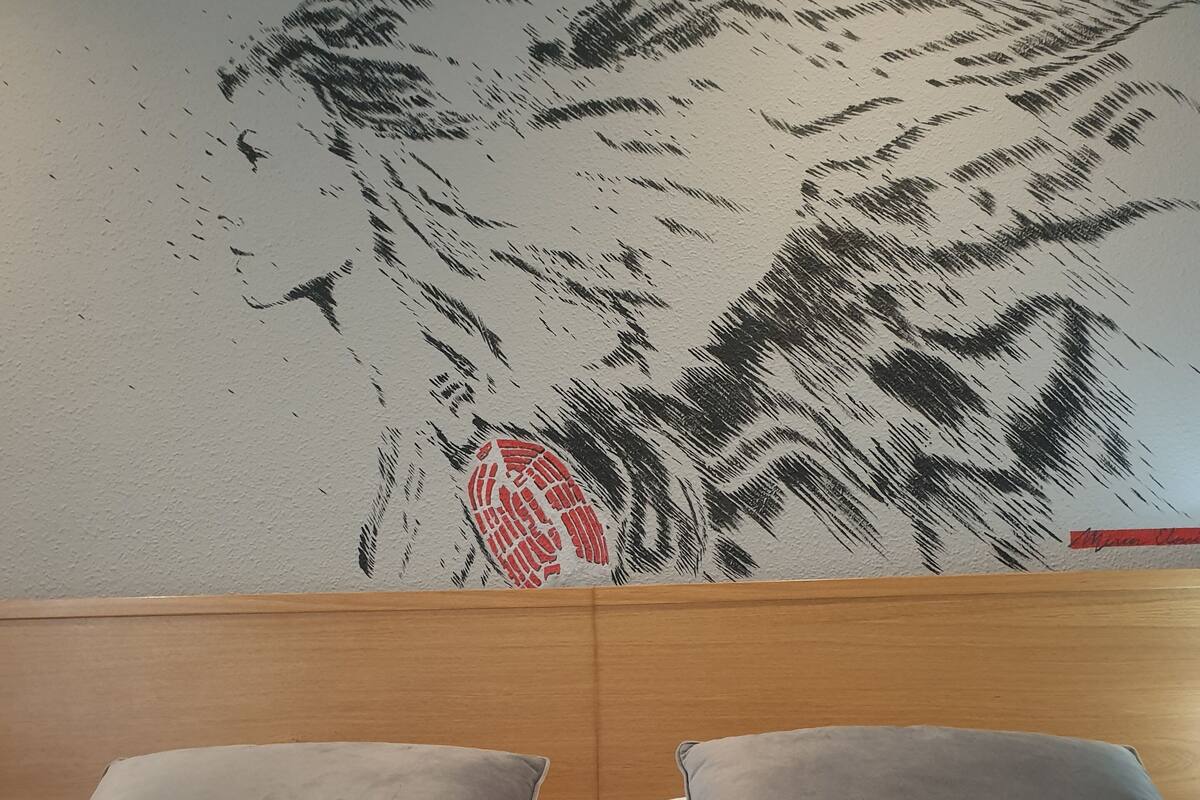 Un llit amb dos coixins gris i un capçal amb mural a la paret.