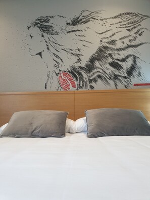 Un lit avec deux oreillers gris et une tête de lit ornée d’une fresque murale.