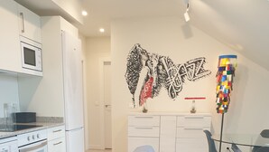 A modern kitchen with white appliances, a grey sofa, and a dining area with a glass table and chairs. - Hotel Arts-Gasteiz (Vitoria-Gasteiz)