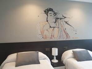 Une chambre d’hôtel avec deux lits, chacun étant équipé d’un oreiller et d’une table de chevet avec une lampe.