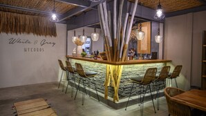 A bar area with a stone wall, wooden bar counter, and several wicker chairs. - White and Grey (Mykonos)
