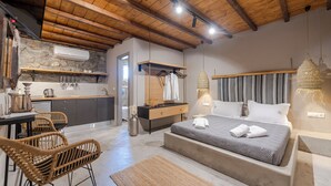 A bedroom with a large bed, a bedside table, and a nightstand. There is a wooden ceiling with exposed beams and a stone wall. - White and Grey (Mykonos)