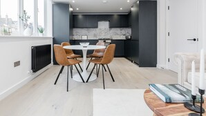 A modern kitchen with dark cabinets, a marble backsplash, and a white dining table with leather chairs. - Perfect Holiday Escape - 1 and 2 Bedroom Deluxe Apartments at Liverpool Street (London)