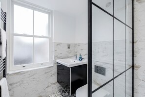 A bathroom with a white sink, black cabinet, and a window with frosted glass.
