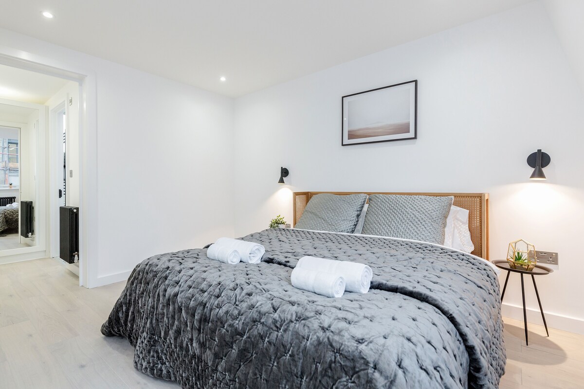 Et moderne soveværelse med en stor seng, en træsenggavl og et lille natbord med en lampe.