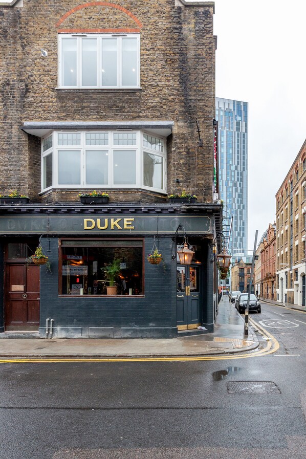 A building with the name "DUKE" on the facade, featuring a black exterior, a large window, and hanging plants.