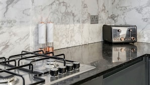 A modern kitchen with a gas stove, stainless steel appliances, marble backsplash, and dark cabinetry. - Perfect Holiday Escape - 1 and 2 Bedroom Deluxe Apartments at Liverpool Street (London)