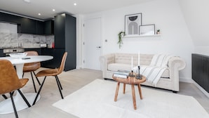 A modern living room with a white sofa, a coffee table, and a dining area with a white table and brown chairs. - Perfect Holiday Escape - 1 and 2 Bedroom Deluxe Apartments at Liverpool Street (London)
