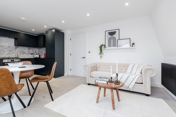 Un salon moderne avec un canapé blanc, une table basse et un coin repas comprenant une table blanche et des chaises marron.