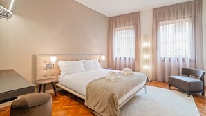 Una camera d'hotel moderna con un letto grande, comodini, una scrivania, una sedia e vista sulla città attraverso ampie finestre.
