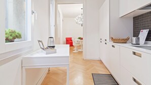 Una cucina moderna con mobili bianchi, una macchina per il caffè e un'area pranzo con una sedia rossa e un tavolo bianco.