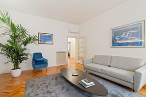 Ein modernes Wohnzimmer mit einer Couch, einem Couchtisch, einem blauen Sessel, einer Zimmerpflanze und Kunstwerken an den Wänden.