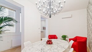 Un'elegante sala da pranzo moderna con tavolo in marmo, sedie rosse, un lampadario e una pianta in vaso.