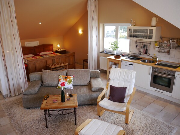 A cozy living room with a sofa, a chair, a small table, and a bed in the background. - Apartment Arras in Bullay / Mosel (Bullay)