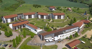 Vista aérea de un hotel con varias construcciones, un patio central y campos verdes circundantes.