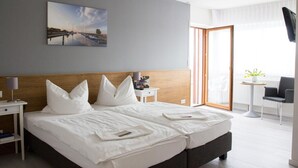 Een hotelkamer met een groot bed, een nachtkastje met een lamp, een klein tafeltje met een plant, en uitzicht buiten via een schuifdeur.