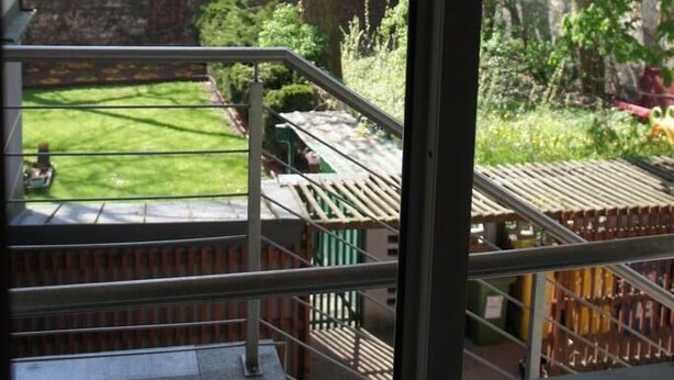 A view from a balcony with a grassy yard, a brick wall, and a tree.