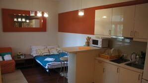A compact room with a bed, a small kitchenette, a dining area, and a sitting area with a chair and a table.