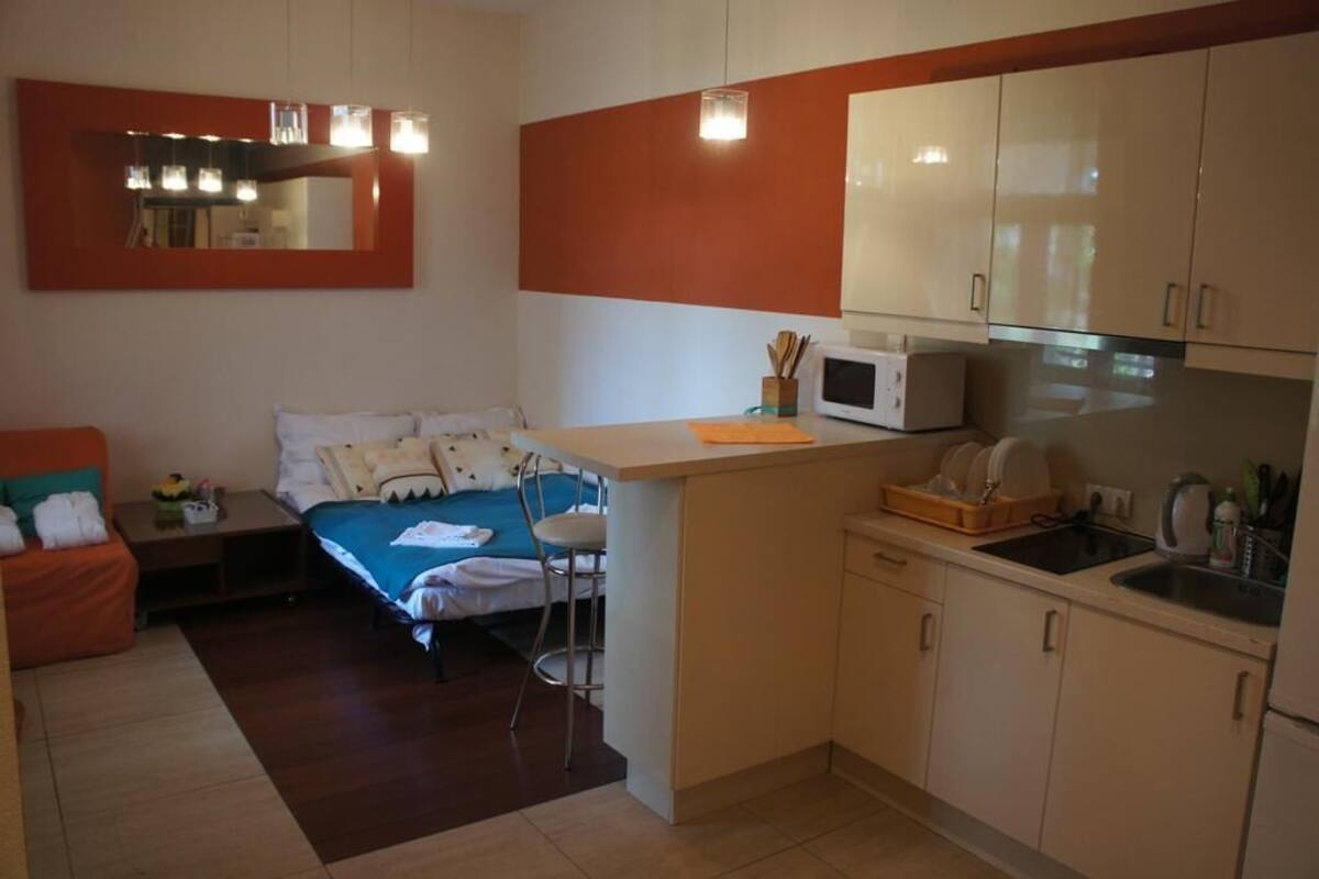 A compact room with a bed, a small kitchenette, a dining area, and a sitting area with a chair and a table.