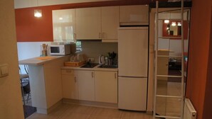 A compact kitchen with white cabinets, a microwave, a refrigerator, and a small sink.